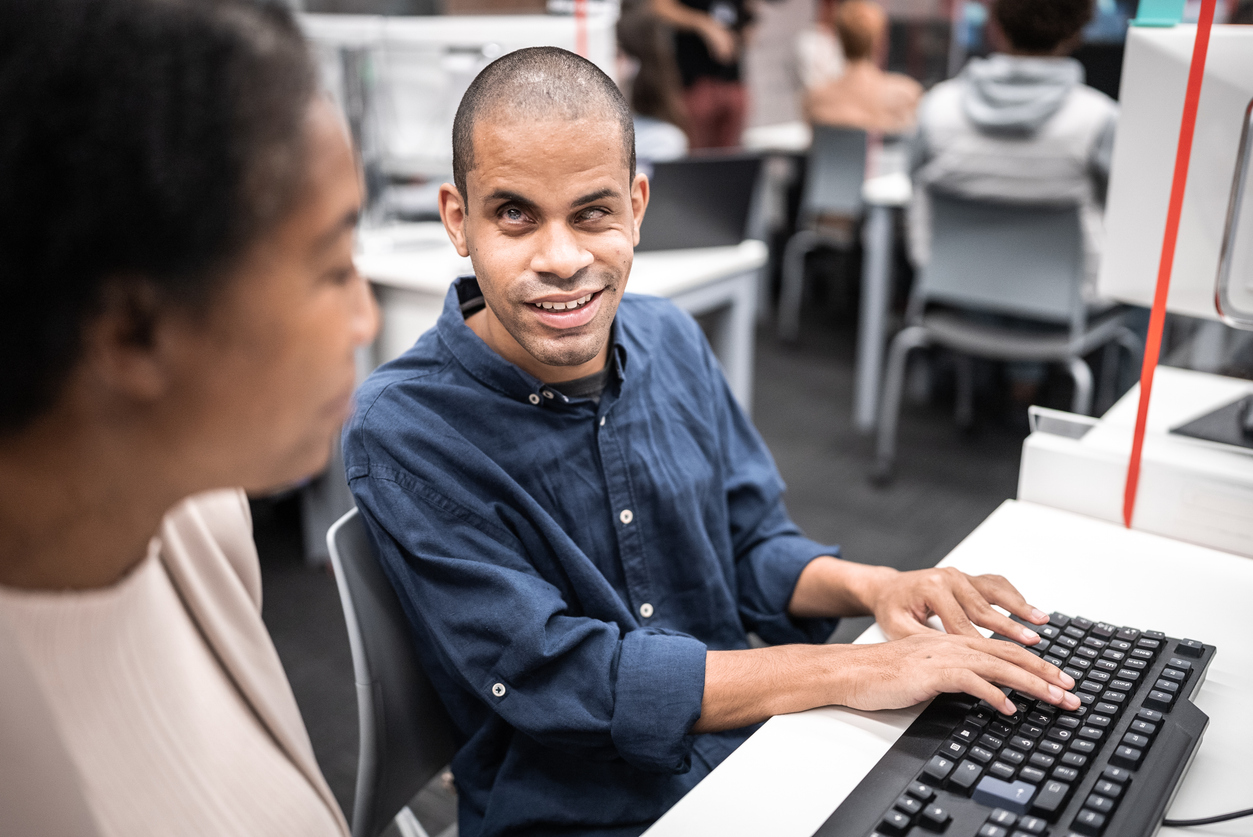 Mature woman support university student (or worker) with visually impaired to use computer at library.
