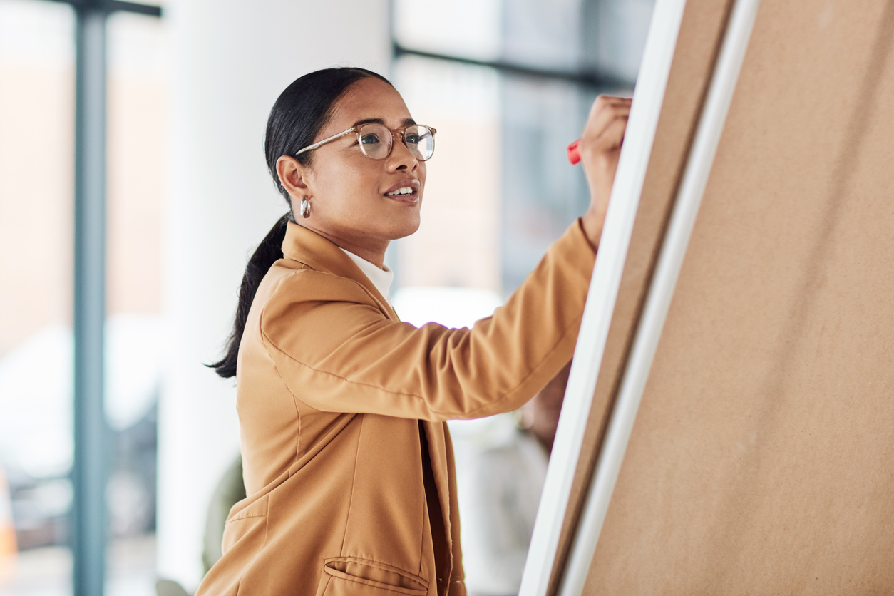 Creative woman, meeting and writing on Flipchart for team building, coaching or activity ideas at office. Happy female employee in presentation using board to write idea or FAQ for company startup