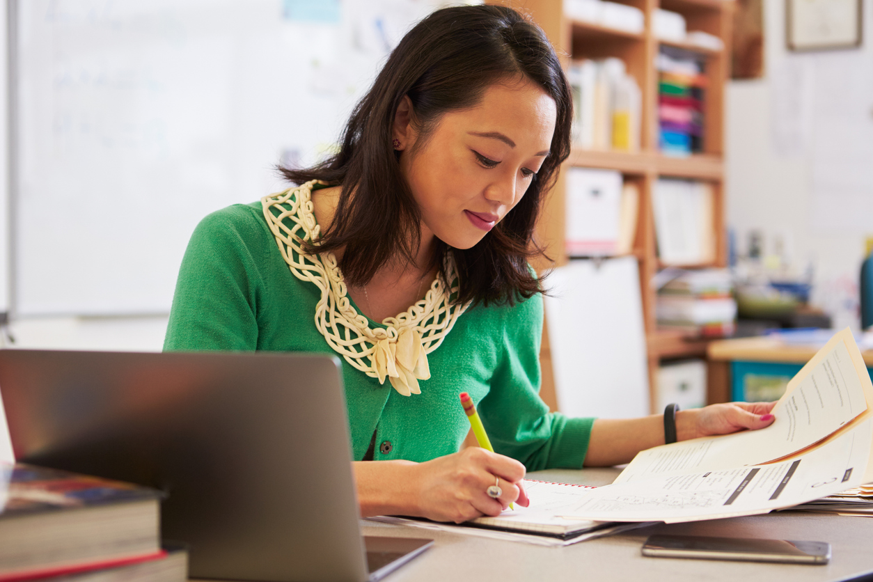 Female Asian teacher working at desk in classroom.