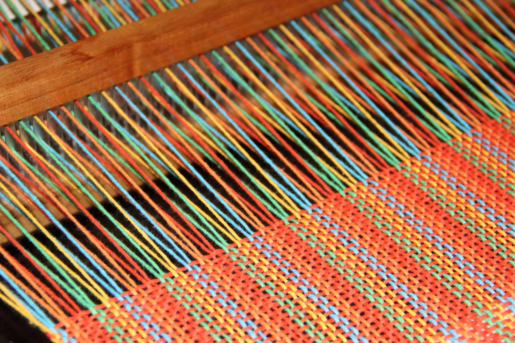 Close up of colorful orange, yellow, blue, and green threads being woven into fabric on a loom.